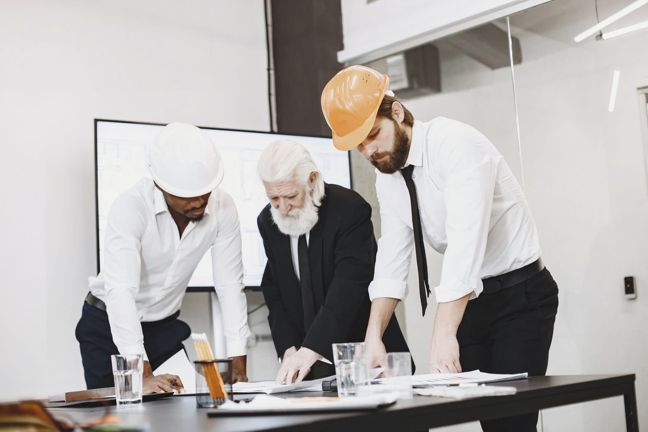 Engineers in hard hats reviewing blueprints around a table