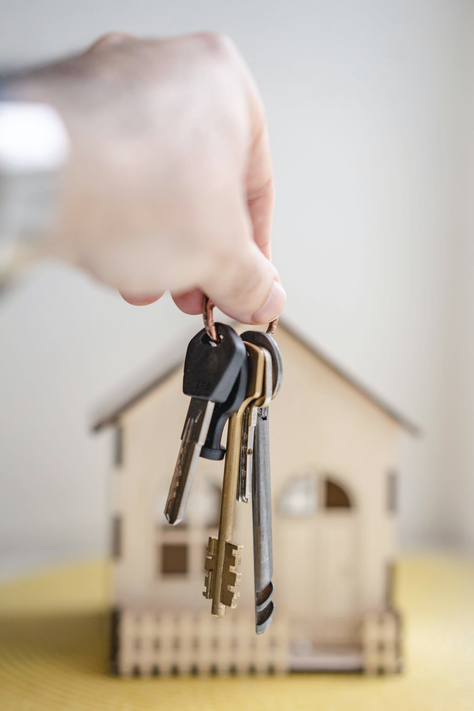 Agent holding house keys beside a wooden house model