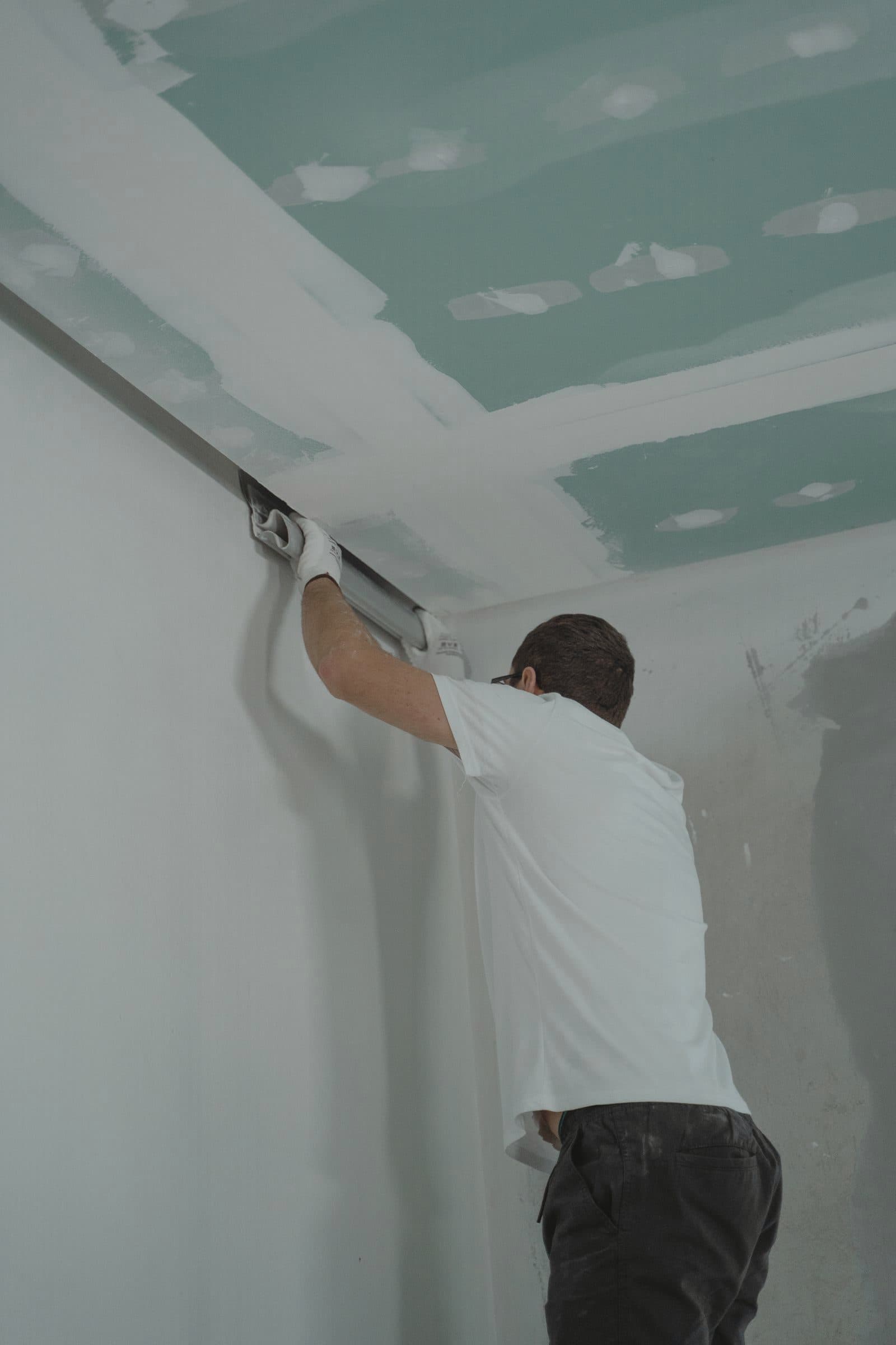 Installer fixing gypsum board ceiling panels in a room under renovation