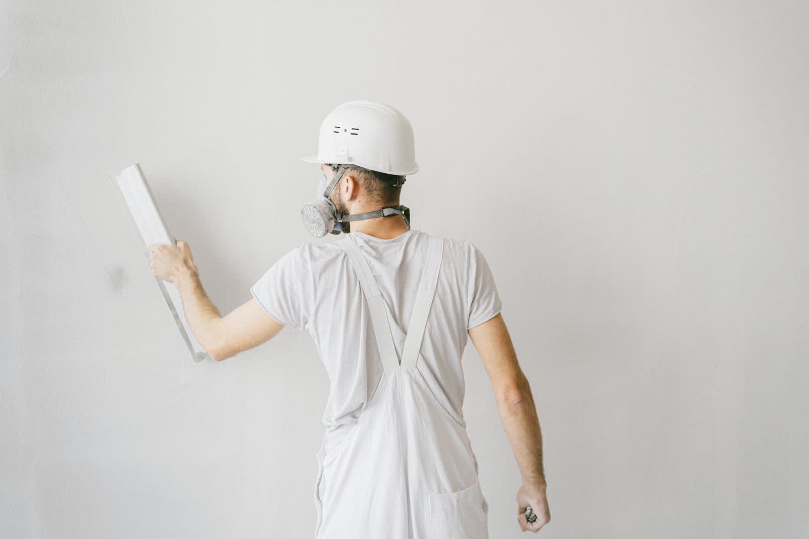 Plasterer in a white hard hat smoothing a fresh plaster wall